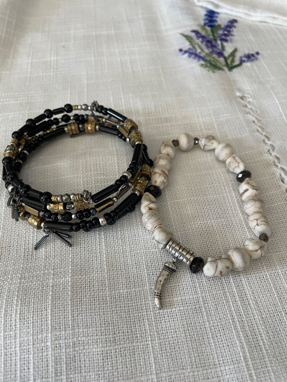 2 bracelets. Black with gold tone adornments. Variegated off white beads.